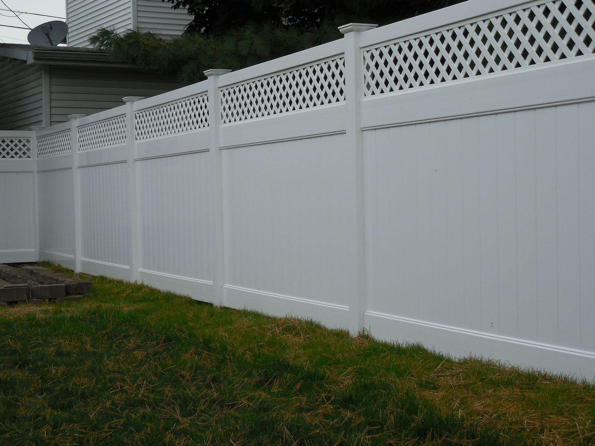 A white fence with a lattice design is in the backyard of a house.
