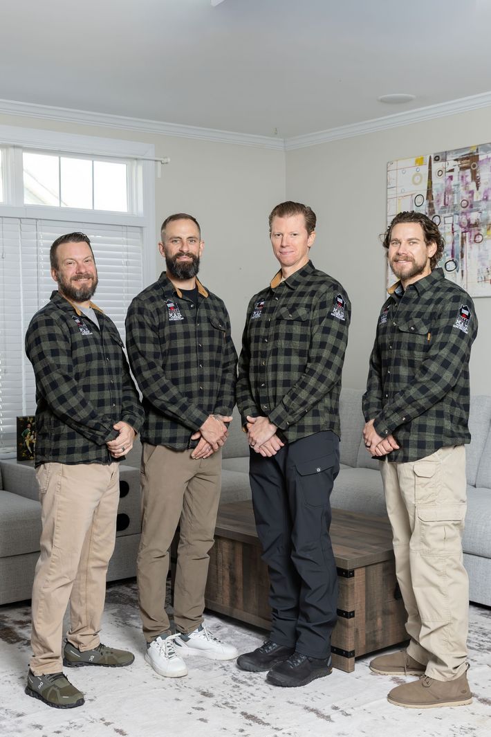 Four people in matching plaid shirts stand in a living room, hands at their sides.