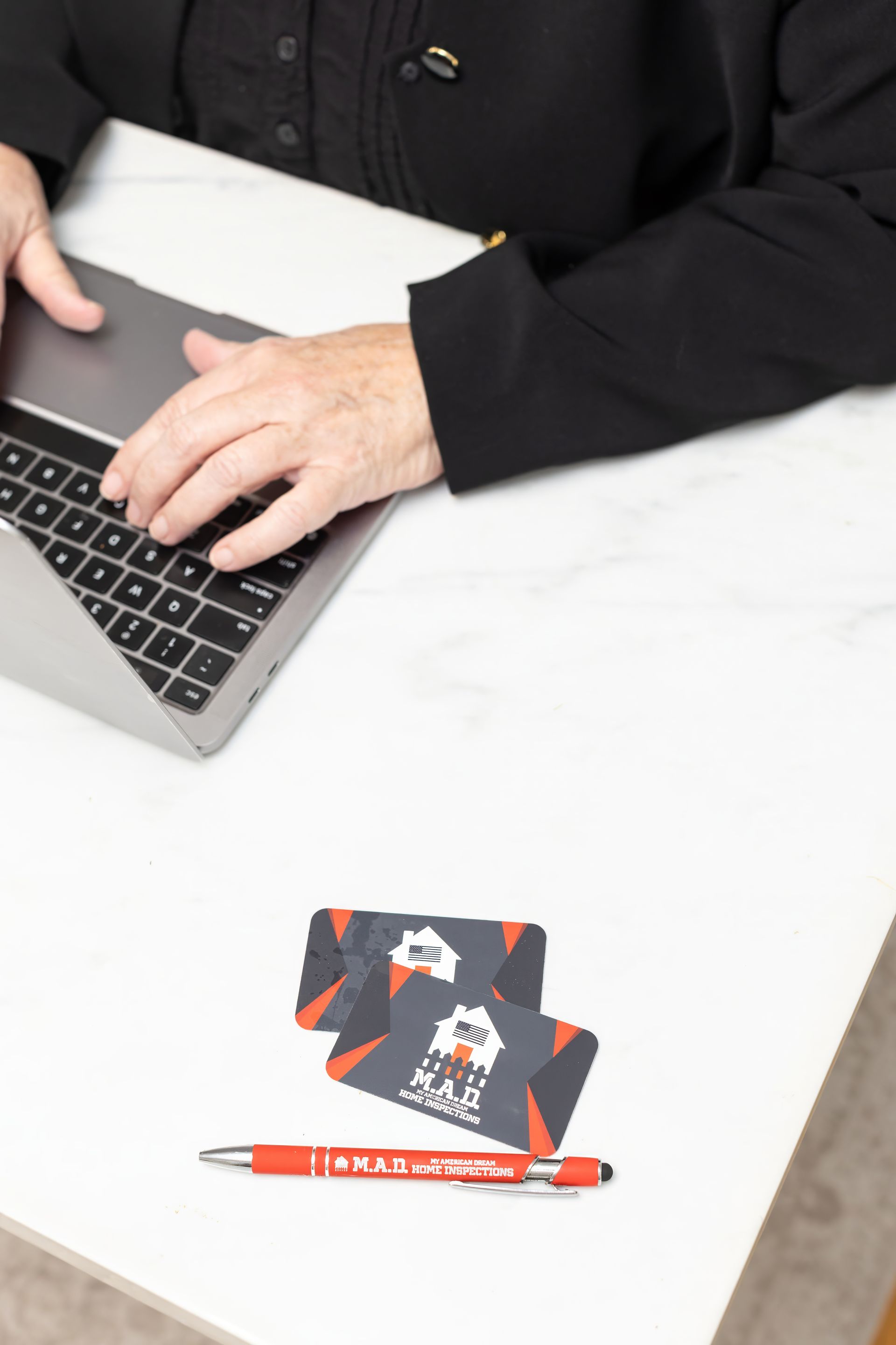 Person typing on laptop at a white table, next to business cards and a pen.