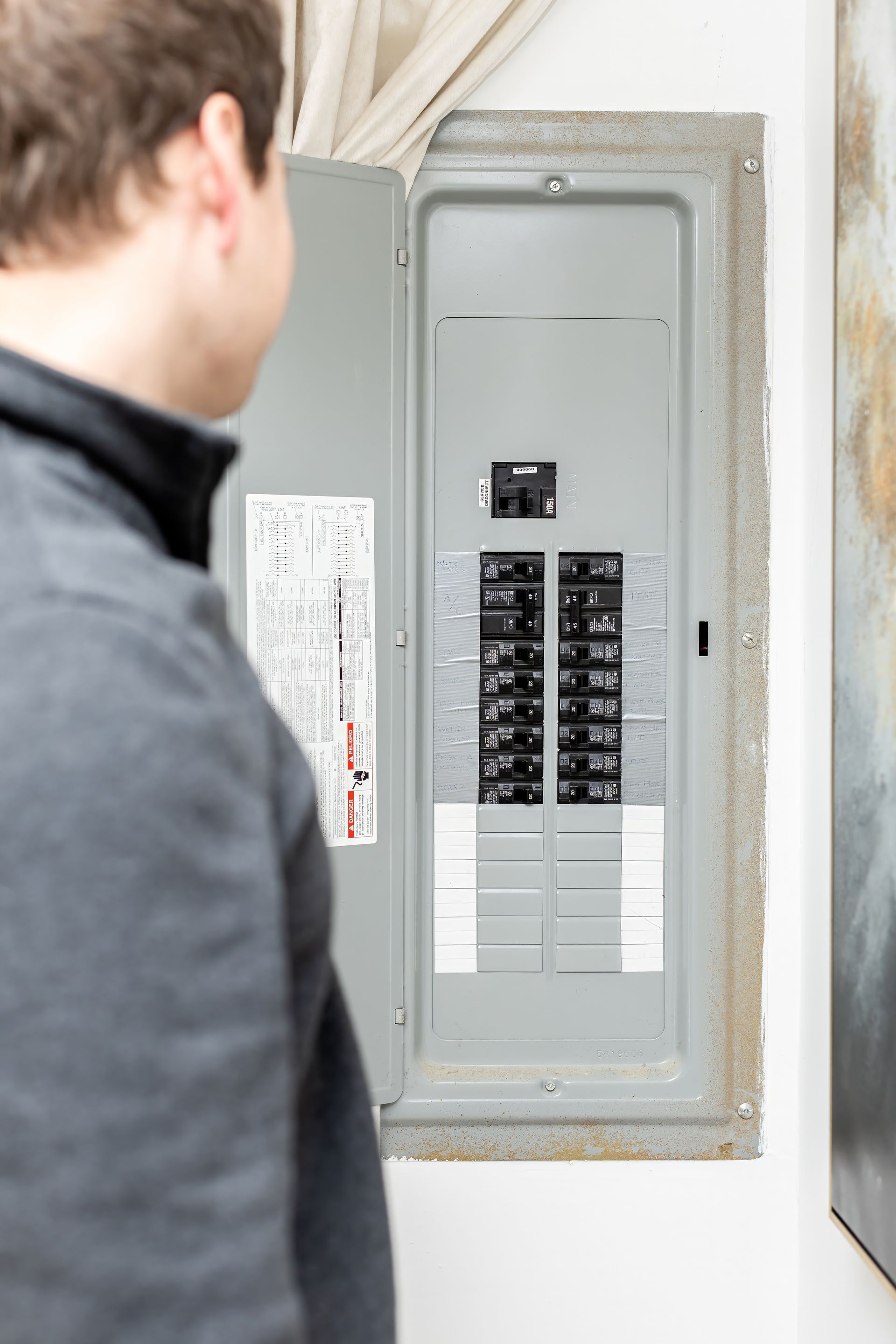 Person looking at an open electrical circuit breaker panel on a wall.