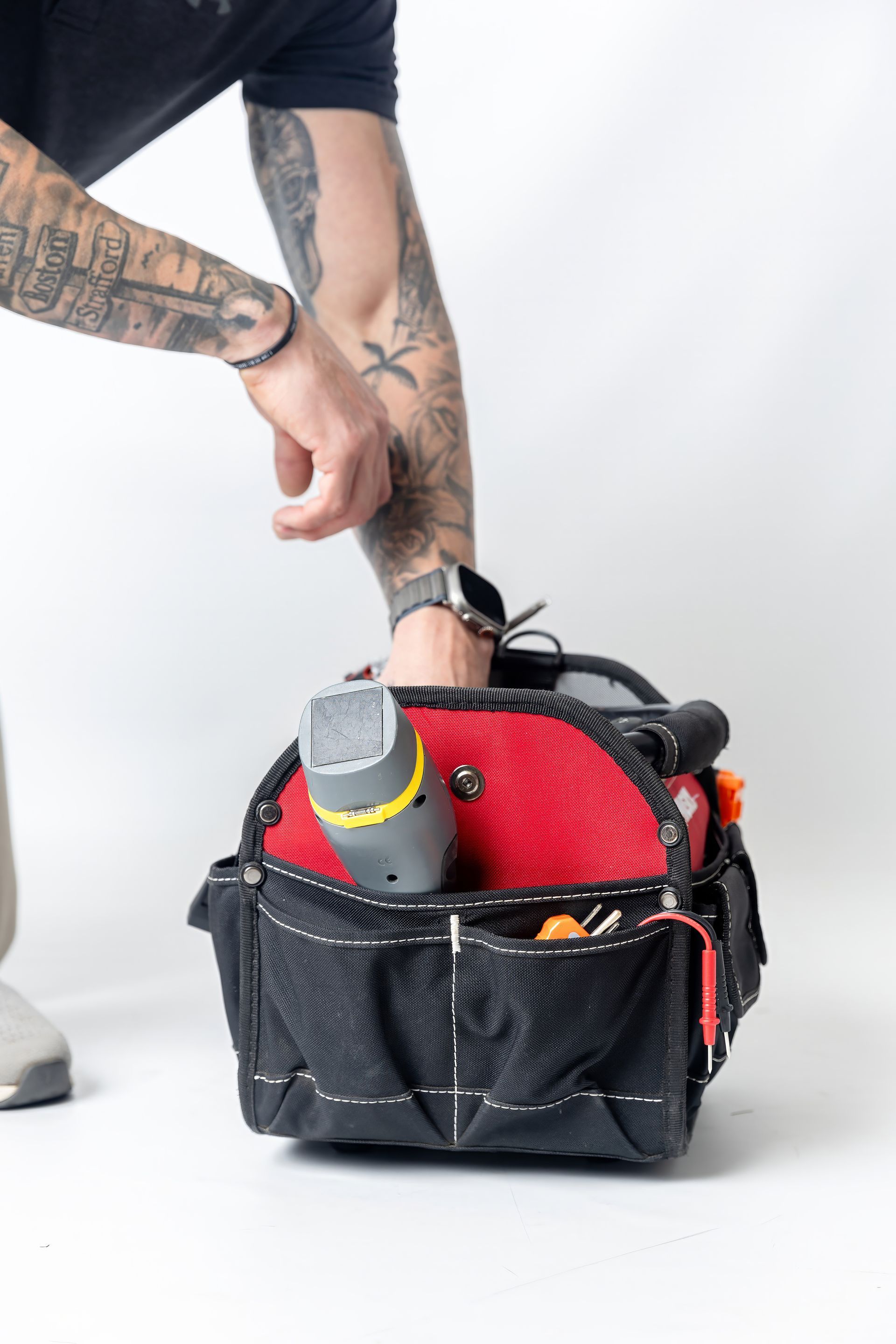 Person reaching into a black and red tool bag. The bag is filled with tools against a white background.