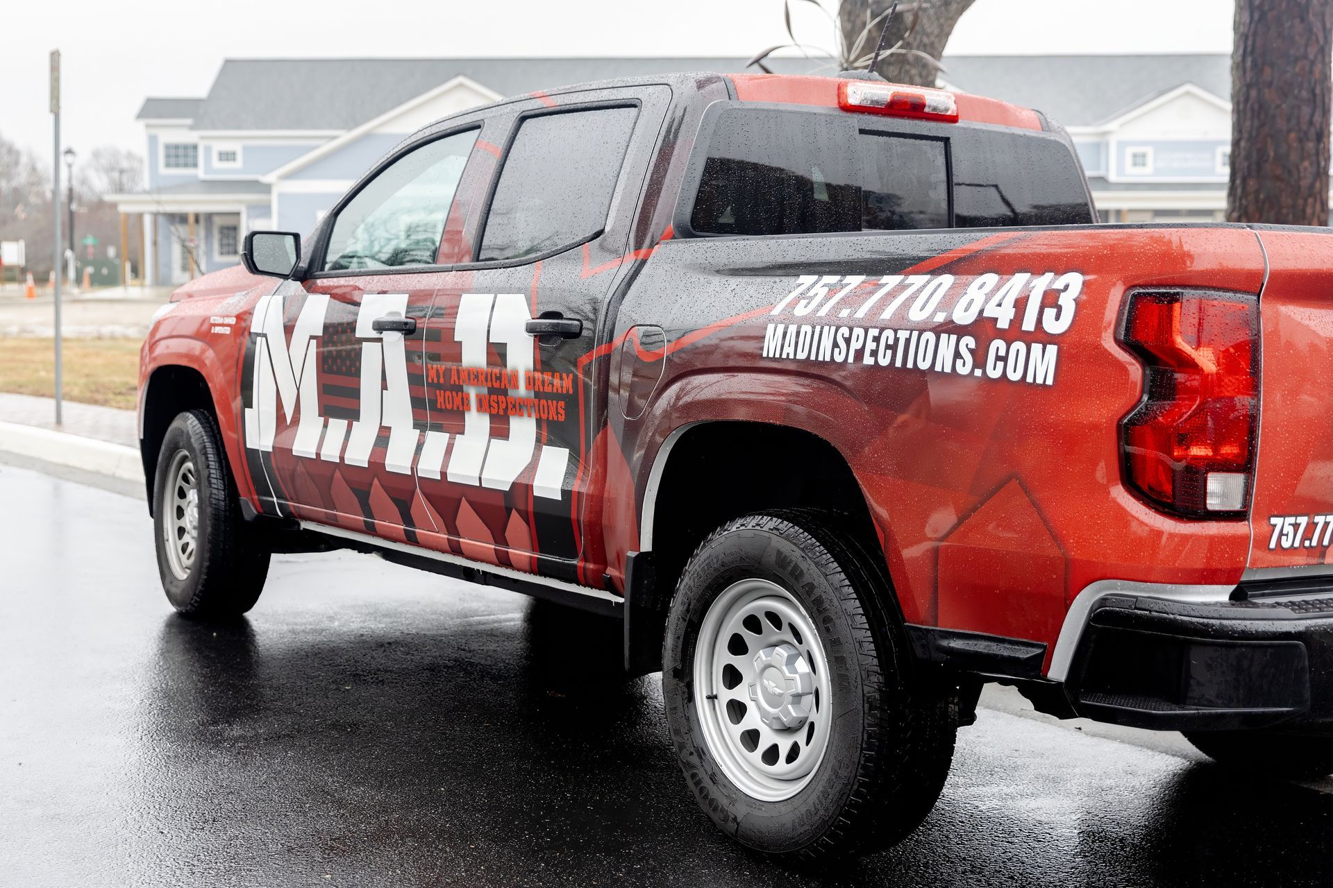 Red pickup truck with business logo parked on wet street.