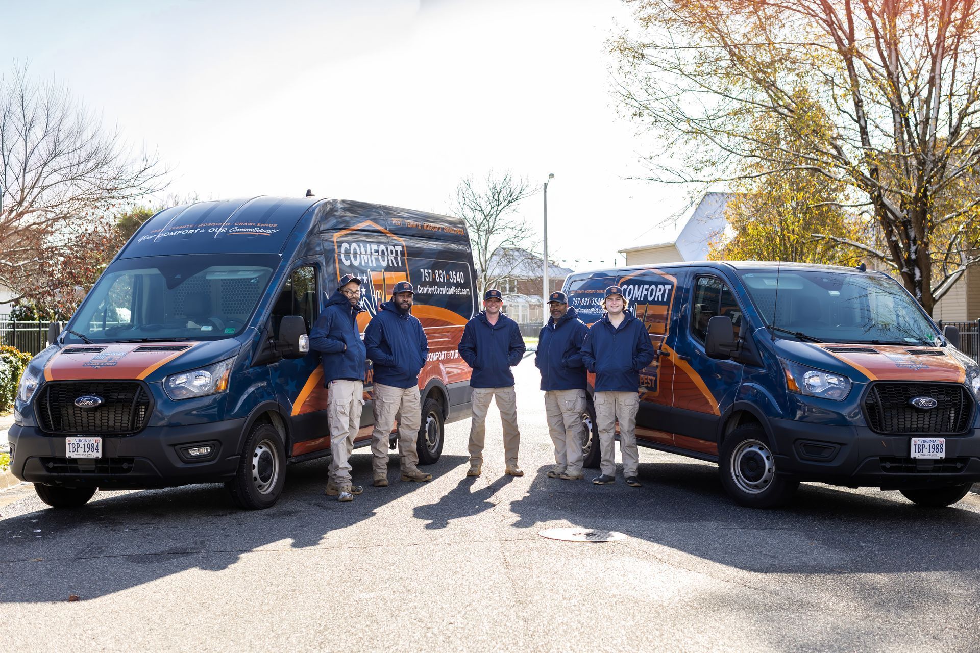 Five people stand near two company vans; vans are blue with orange accents.