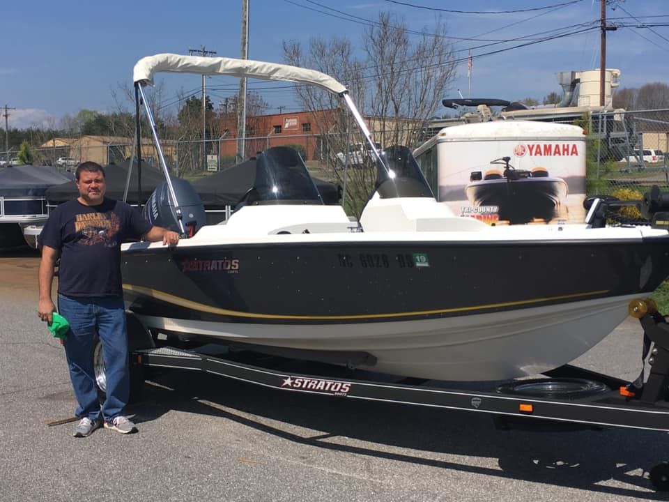 Man stands next to a black and white Yamaha boat on a trailer. He's holding a green object.