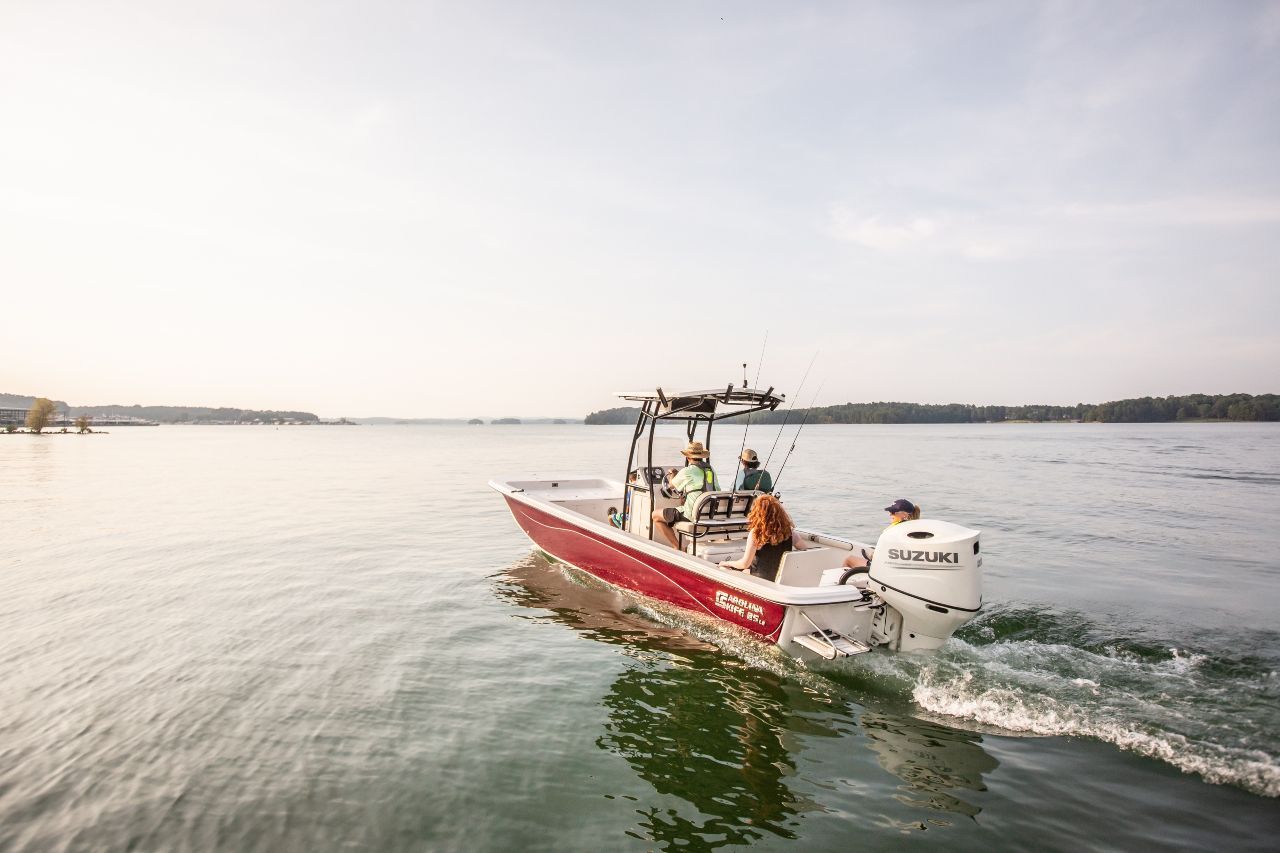 Red and white motorboat with three people on calm water, near a shoreline.