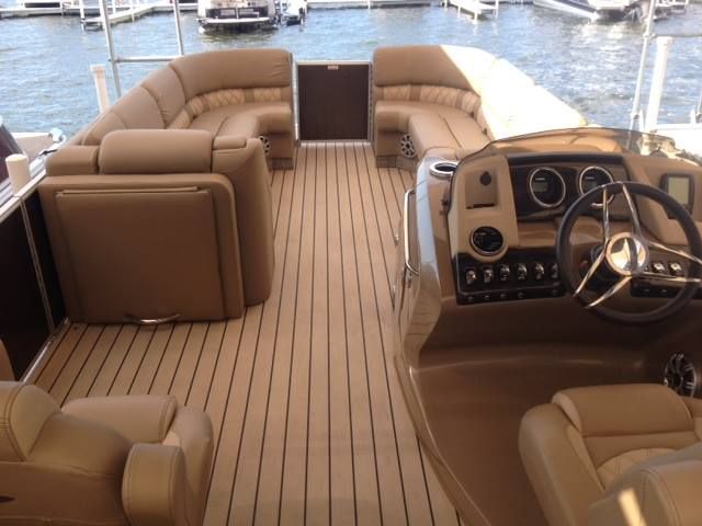 Interior of a pontoon boat with tan seating, wooden floors, and a steering wheel.