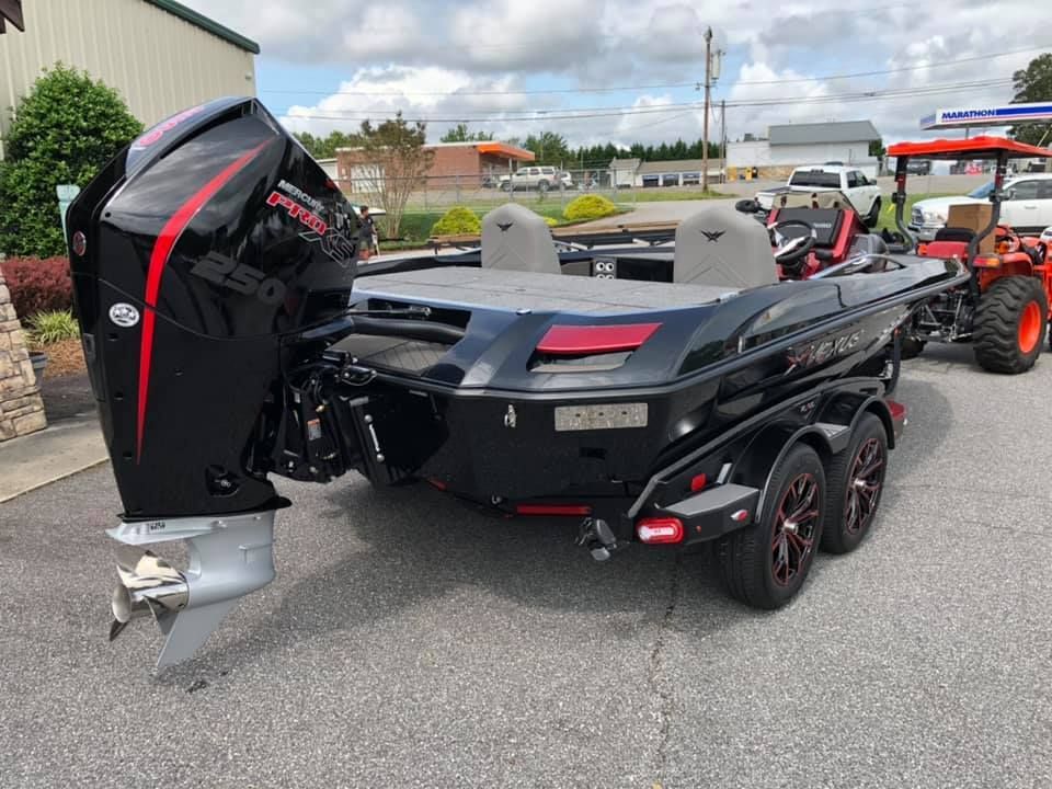 Black bass boat with a large motor on a trailer in a parking lot.