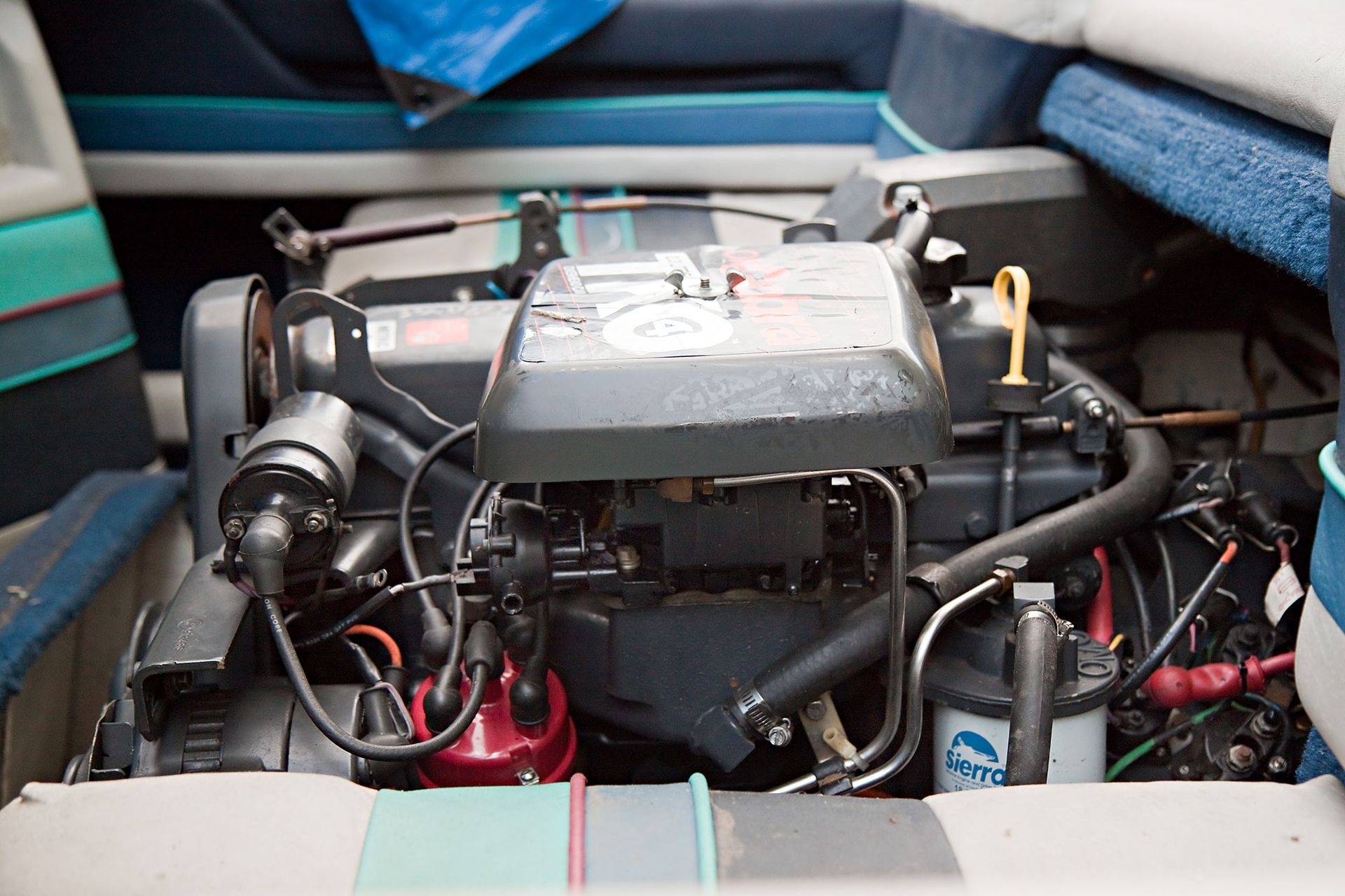 Marine engine in a boat, black and red components, yellow oil cap, surrounded by blue and white upholstery.