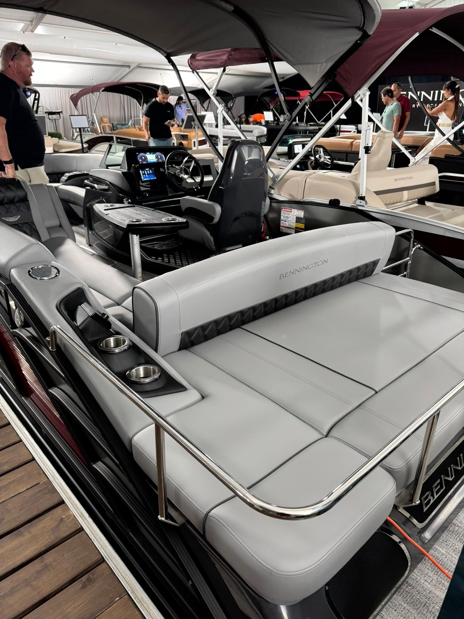 Gray pontoon boat interior with seating, console, and people in a showroom.