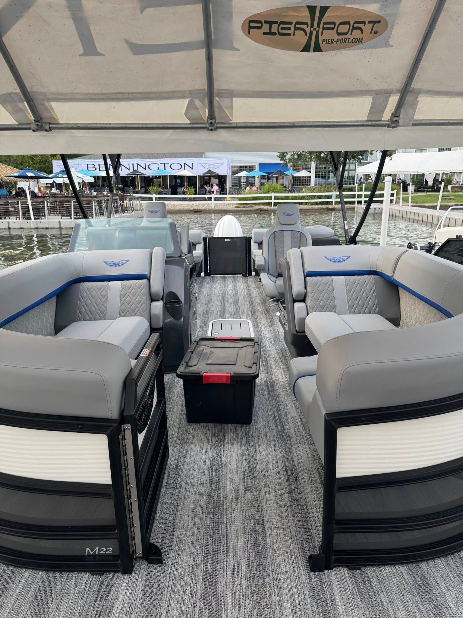 Interior of a pontoon boat with gray seating, black accents, and a weathered wood floor, under a white canopy.