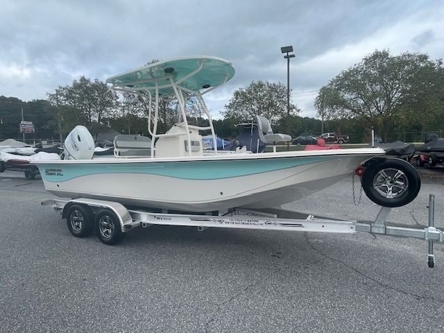 White and turquoise center console boat on a trailer, under a cloudy sky.