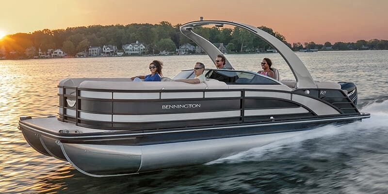 A pontoon boat with four people on a lake at sunset.