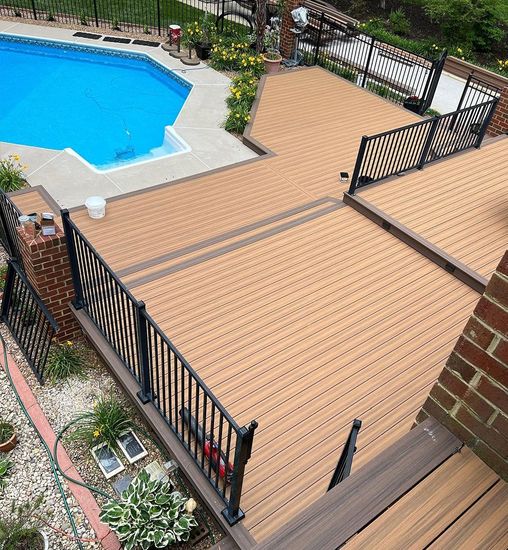 Wooden pool deck with black railings beside a blue swimming pool and garden plants