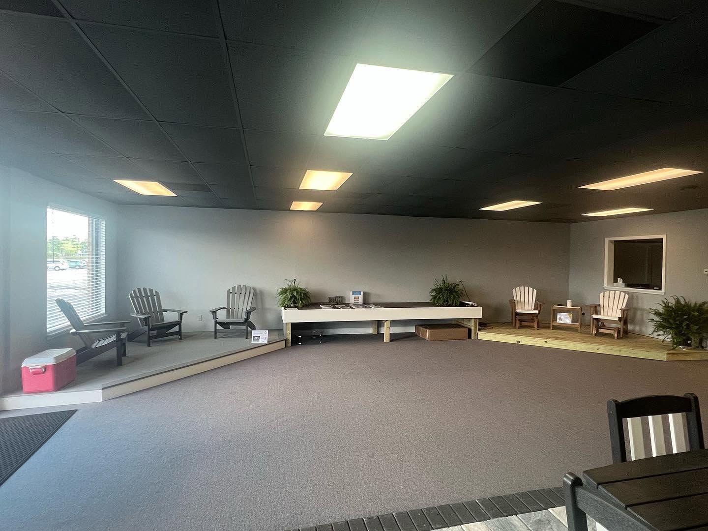 Empty event room with carpet, stage platform, chairs, tables, and fluorescent ceiling lights.