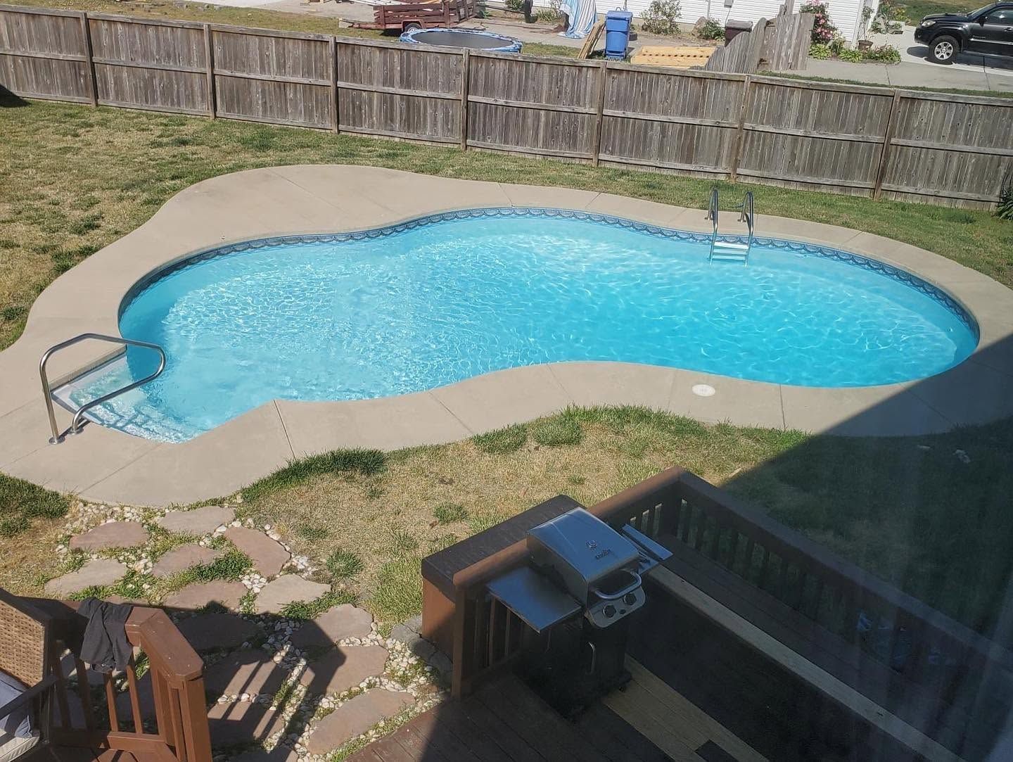 Backyard swimming pool with bright blue water, patio, and wooden fence surrounding it