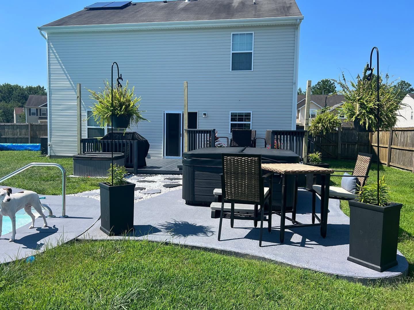 Backyard patio with table, chairs, potted plants, and a dog near a white house
