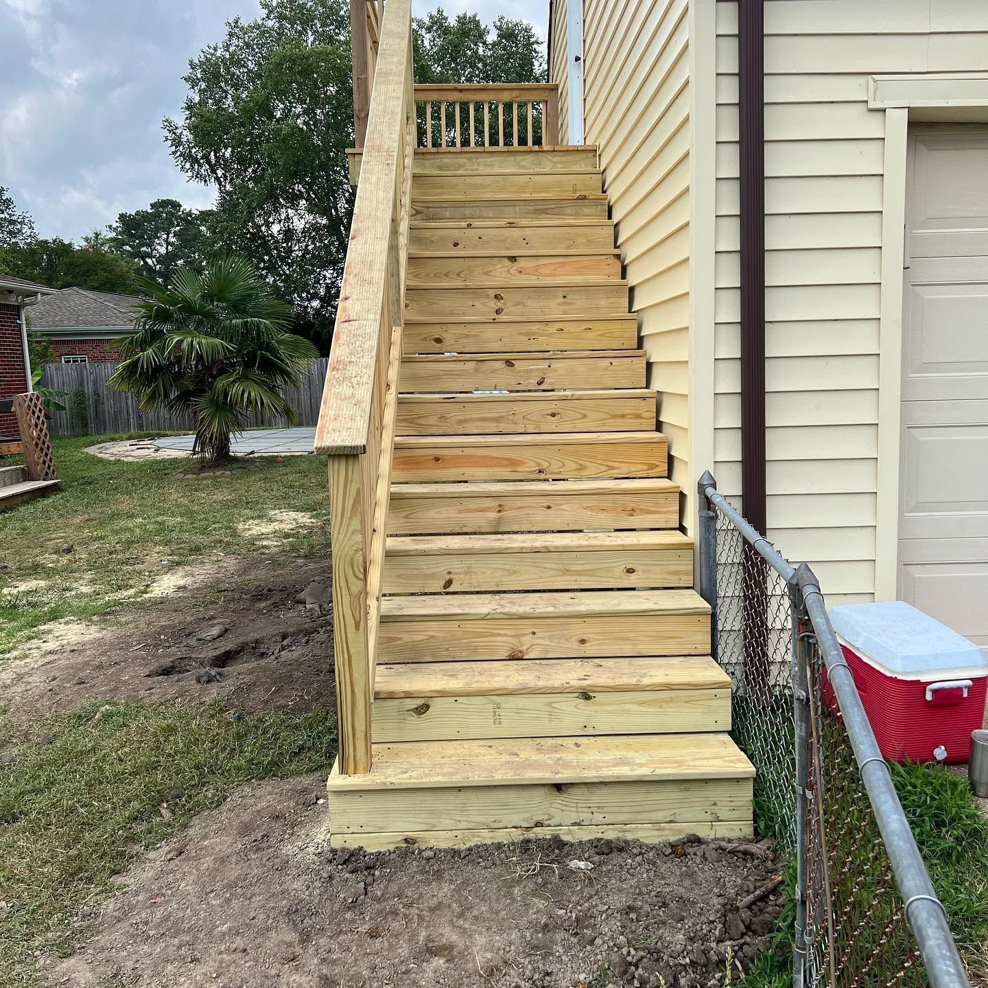 Outdoor wooden staircase beside a house, with a handrail and gravel yard below