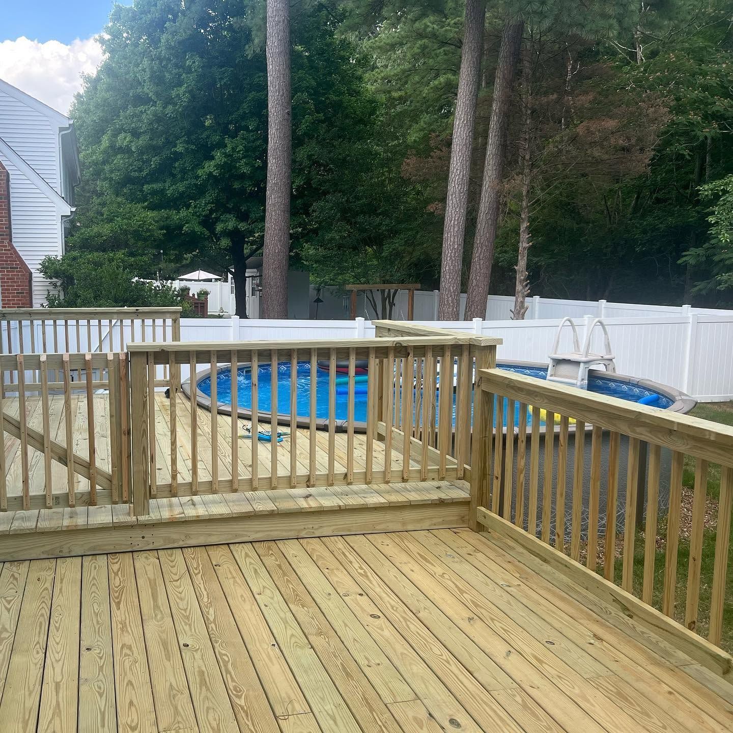 Wooden deck with railings overlooking an above-ground pool in a wooded backyard