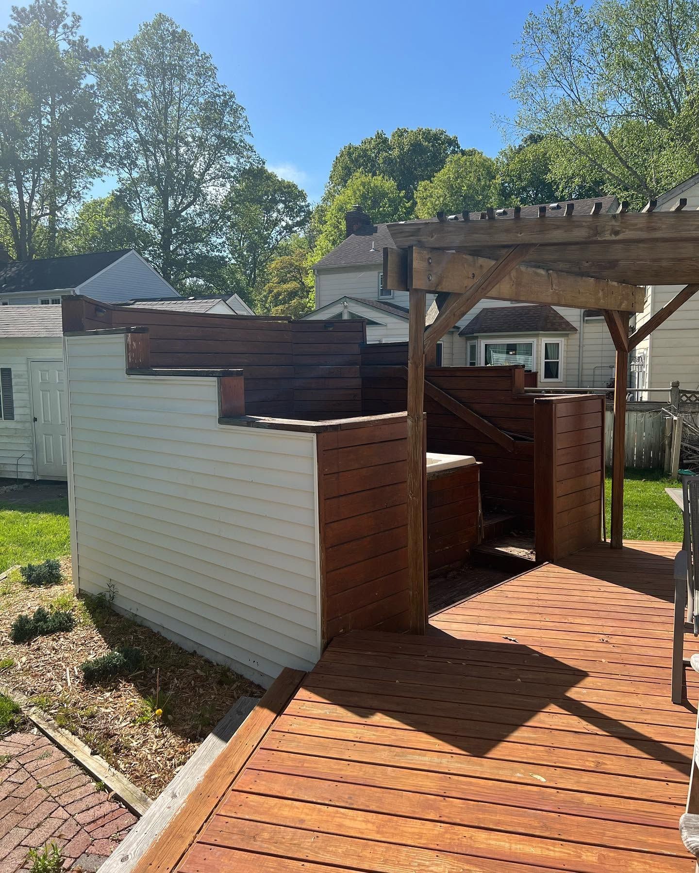 Backyard wooden deck and pergola beside a white shed, with trees and houses in the background