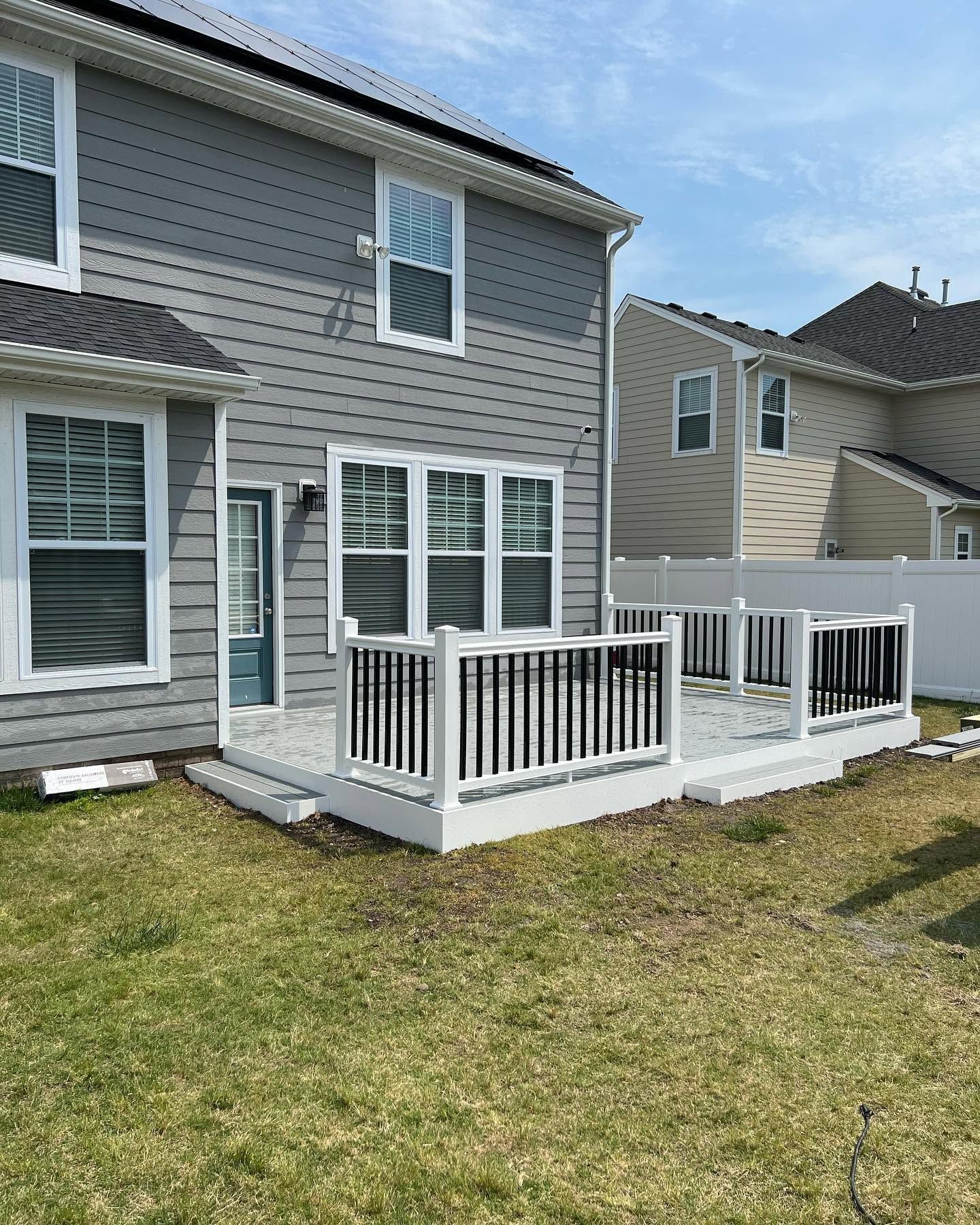 Backyard deck with white railings attached to a gray two-story house under a blue sky