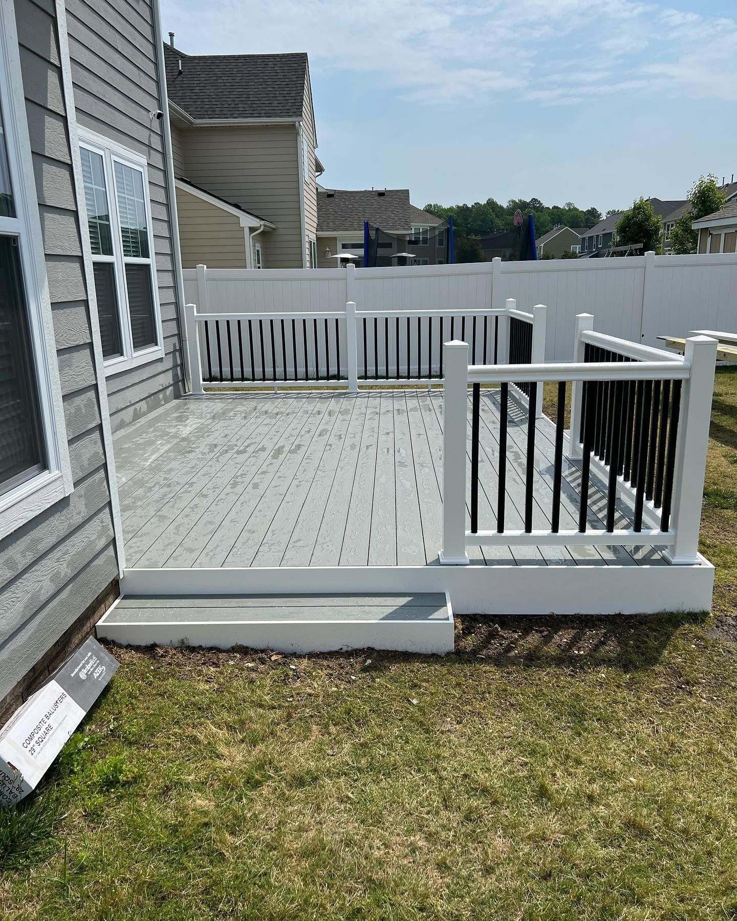 White wooden deck with railing beside a house, overlooking a fenced backyard lawn.