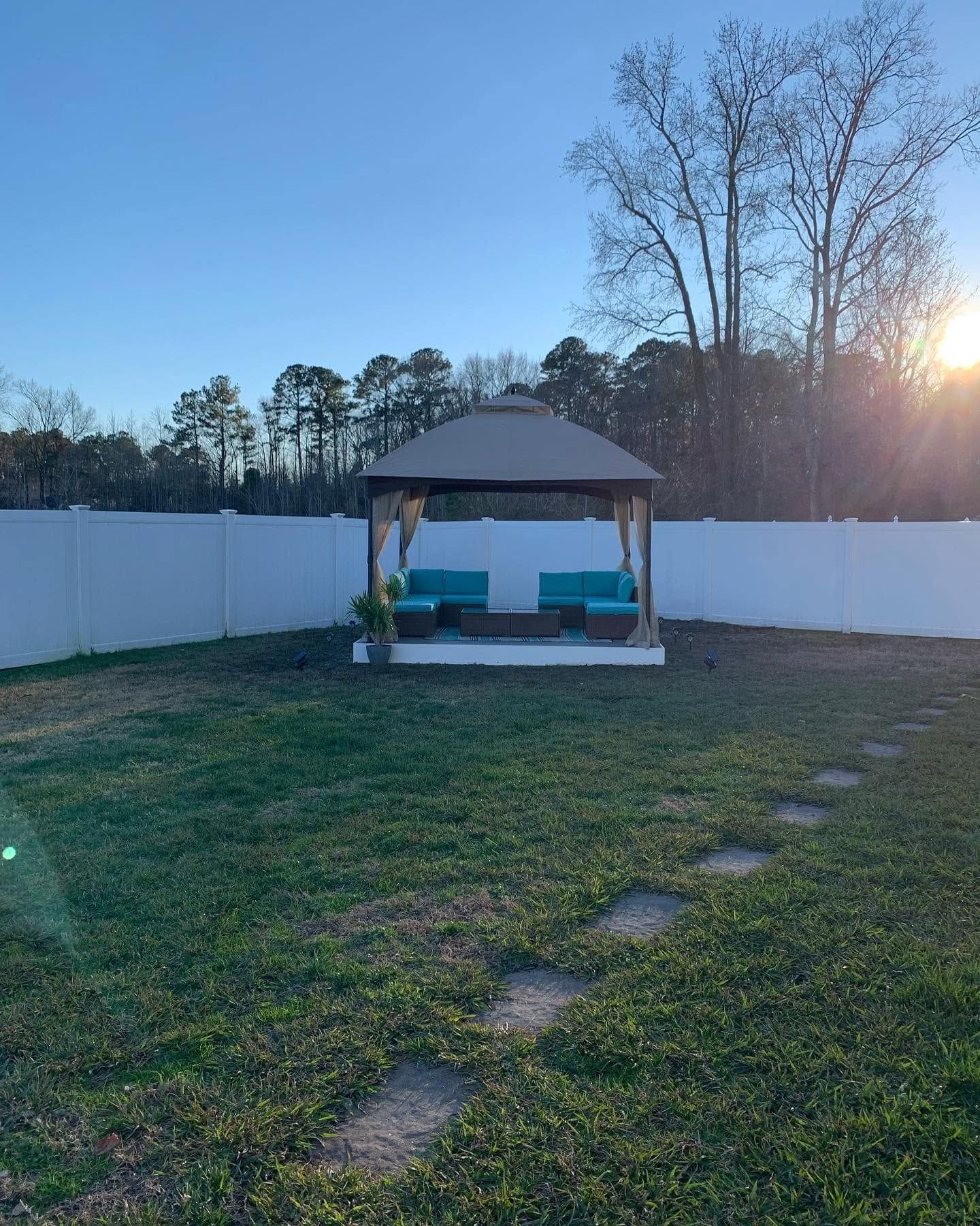 Backyard gazebo with teal bench, white fence, and setting sun over grassy lawn