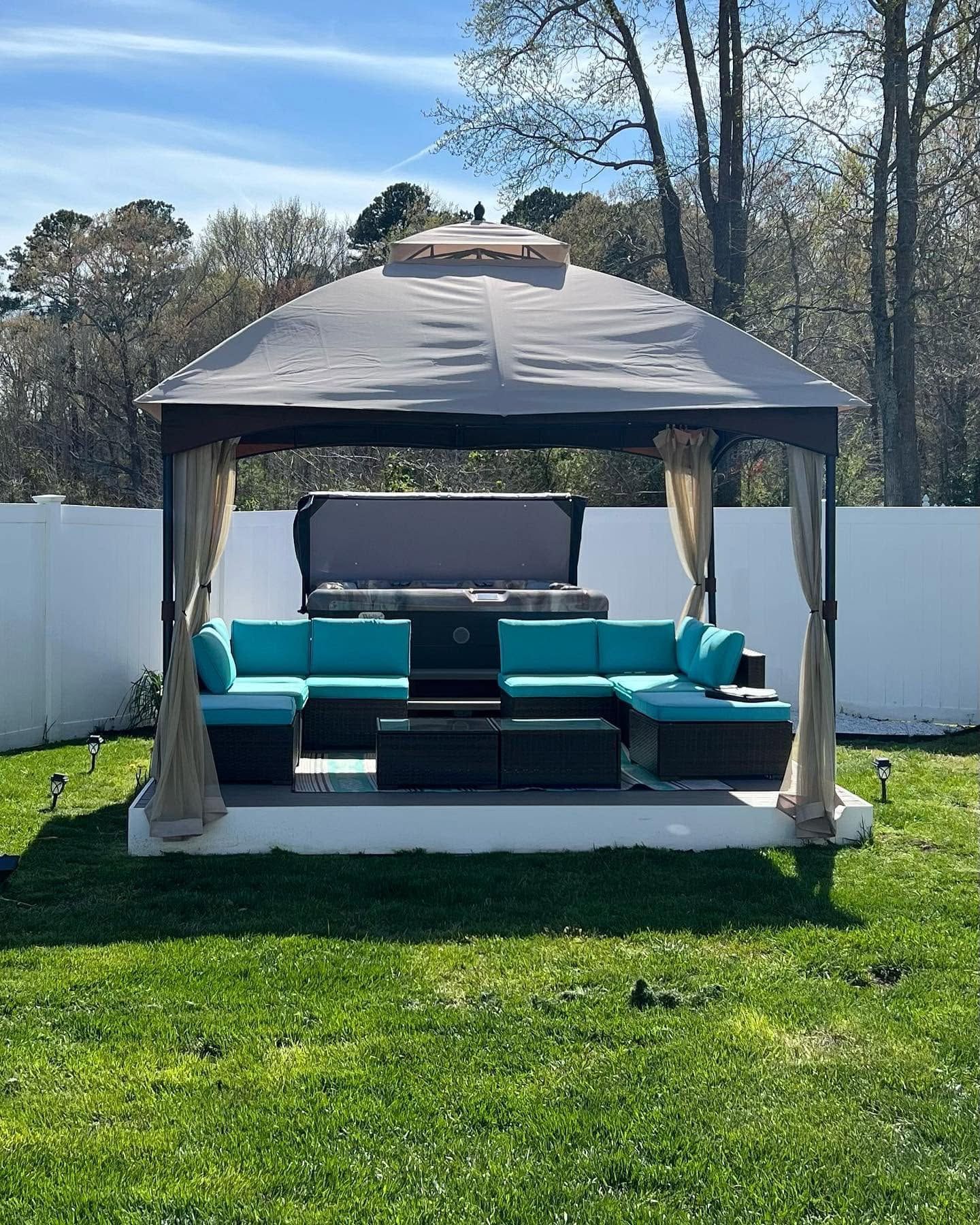 Gray gazebo with teal patio seating on a green lawn in a fenced backyard, sunny day
