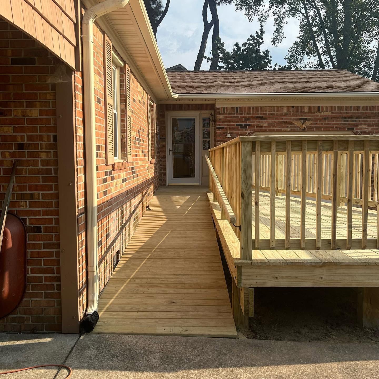 Wooden ramp walkway beside a brick house leading to a back door, with a raised deck on the right.
