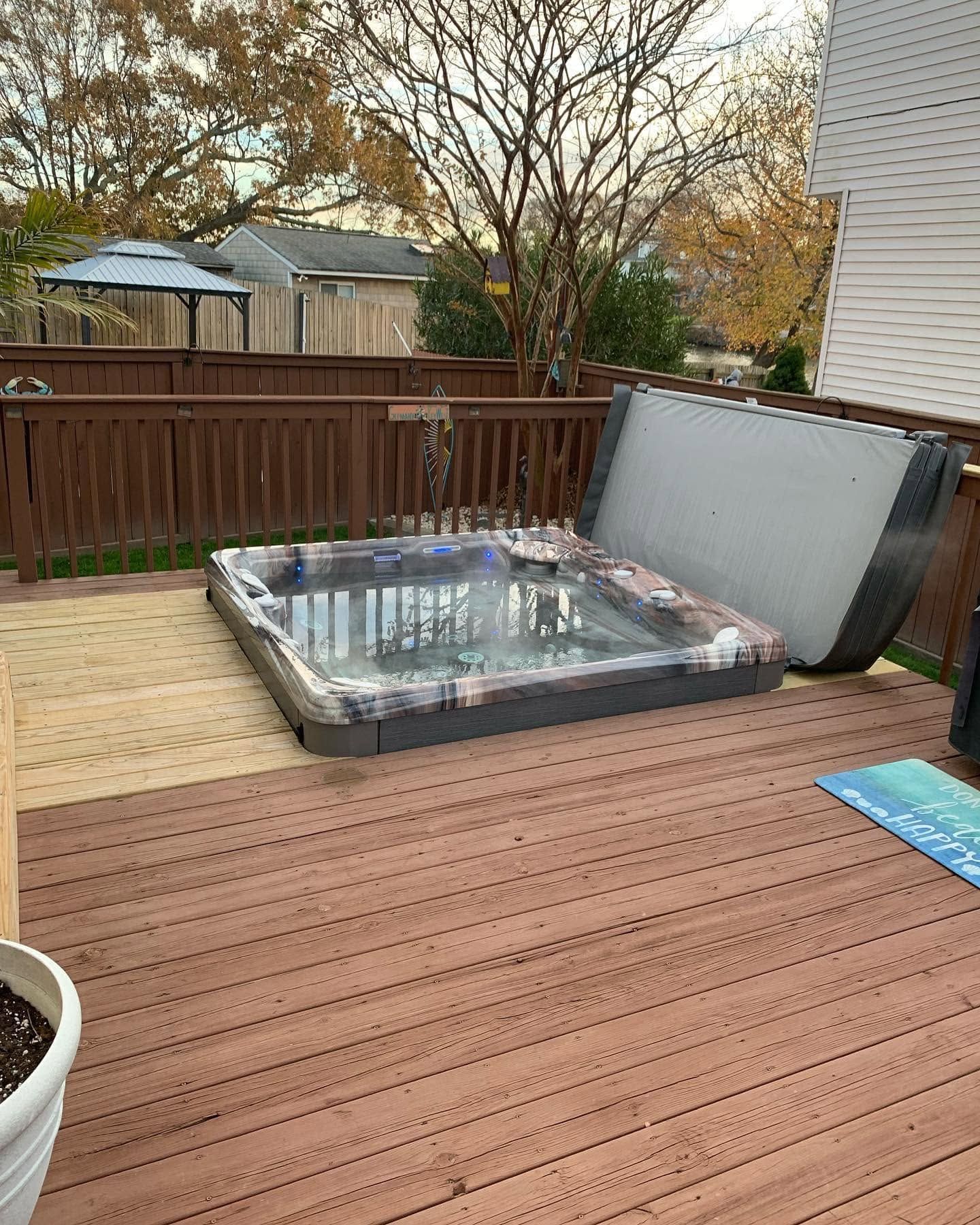 Backyard deck with a small hot tub or spa beside a wooden fence and autumn trees