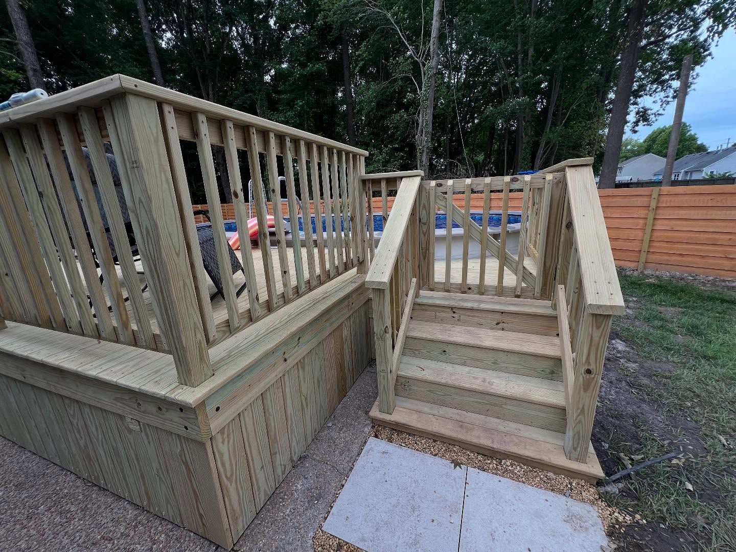 Wooden deck stairs with railing beside a fenced backyard, showing fresh lumber construction.