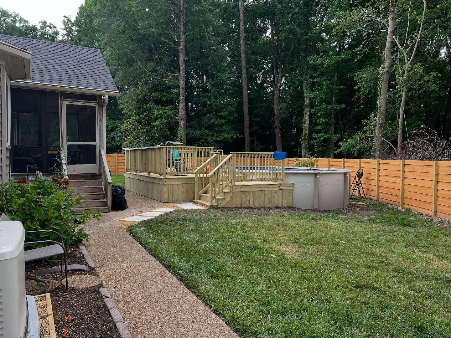 Backyard with a wooden deck, gravel path, lawn, and fenced patio area beside a house