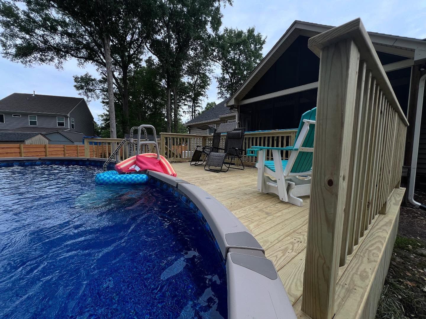 Backyard pool beside a deck and patio chairs, with a pink and blue float on the water