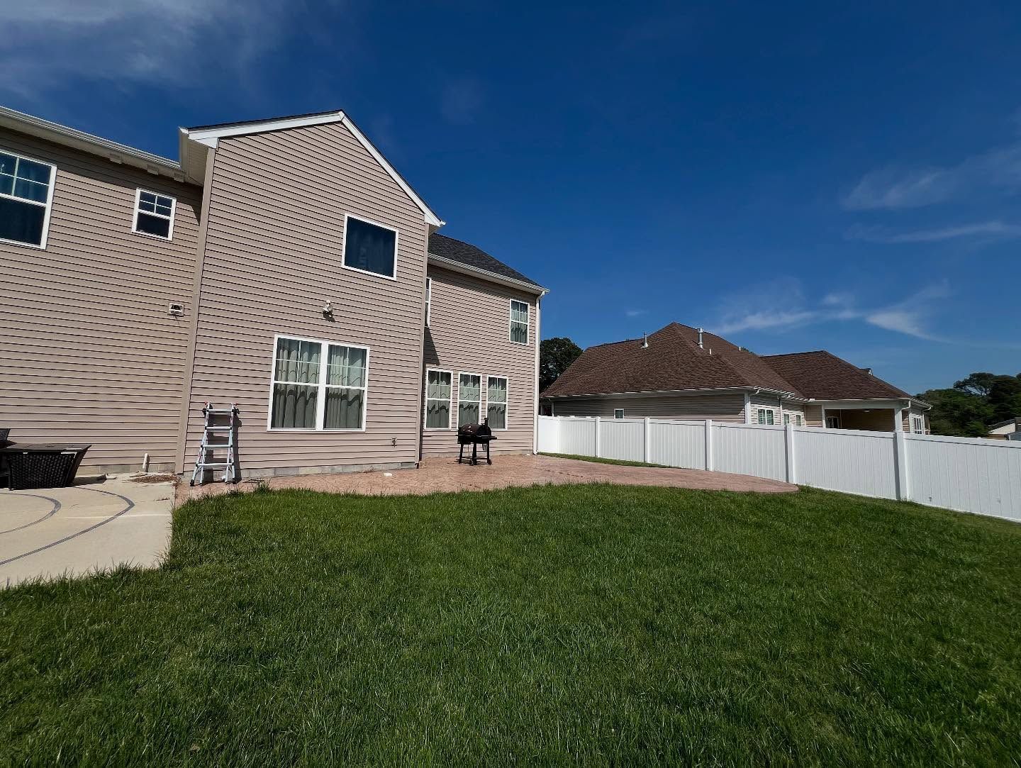 Backyard view of a beige house with green lawn, white fence, and blue sky