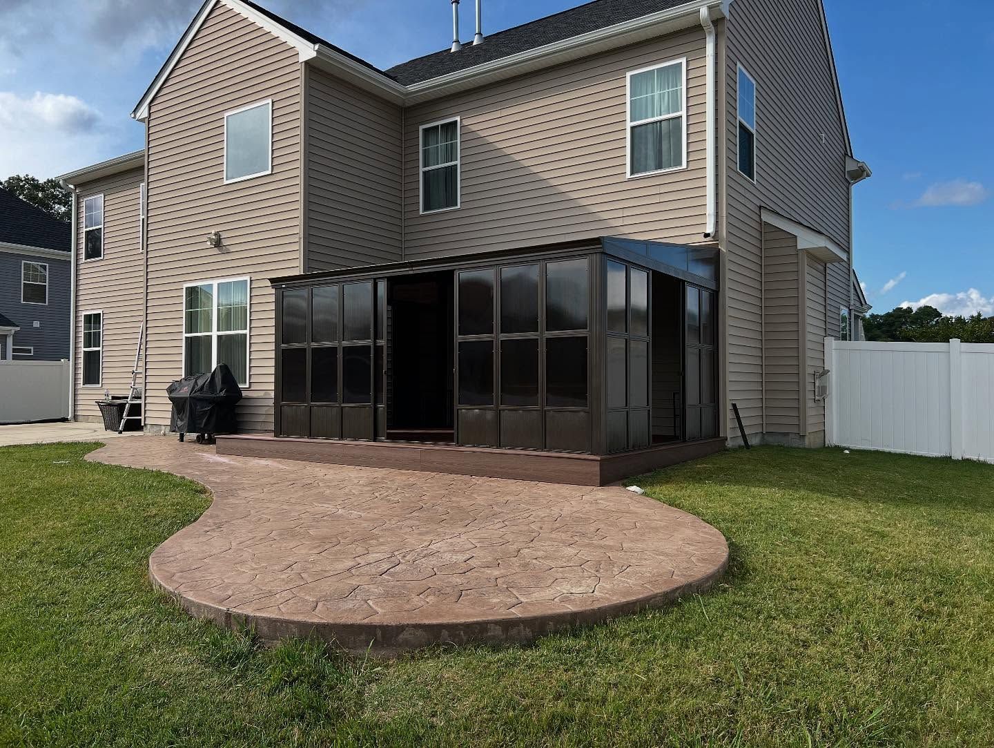 Backyard view of a two-story house with a screened patio and a round mulch bed on the lawn