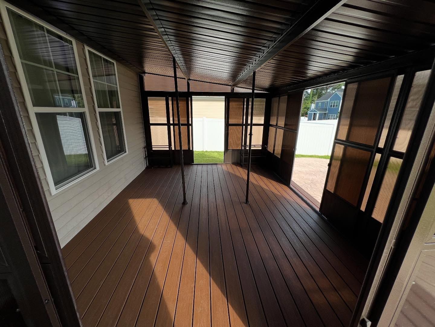 Empty screened porch with wood floor, dark ceiling, and sunlight streaming through open windows.