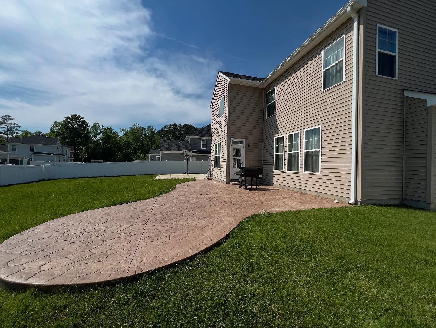 Backyard patio beside a brick house with a curved gravel path and green lawn under a blue sky