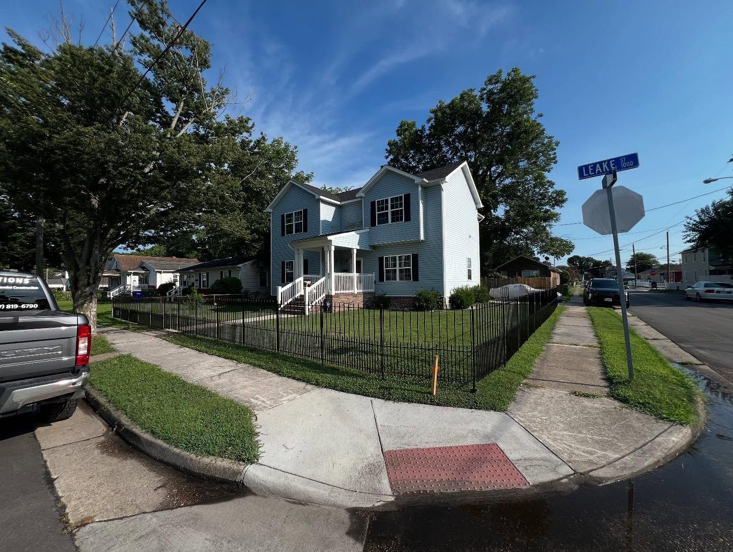 Residential house with white siding and black shutters on a corner lot with a fenced yard and sidewalk