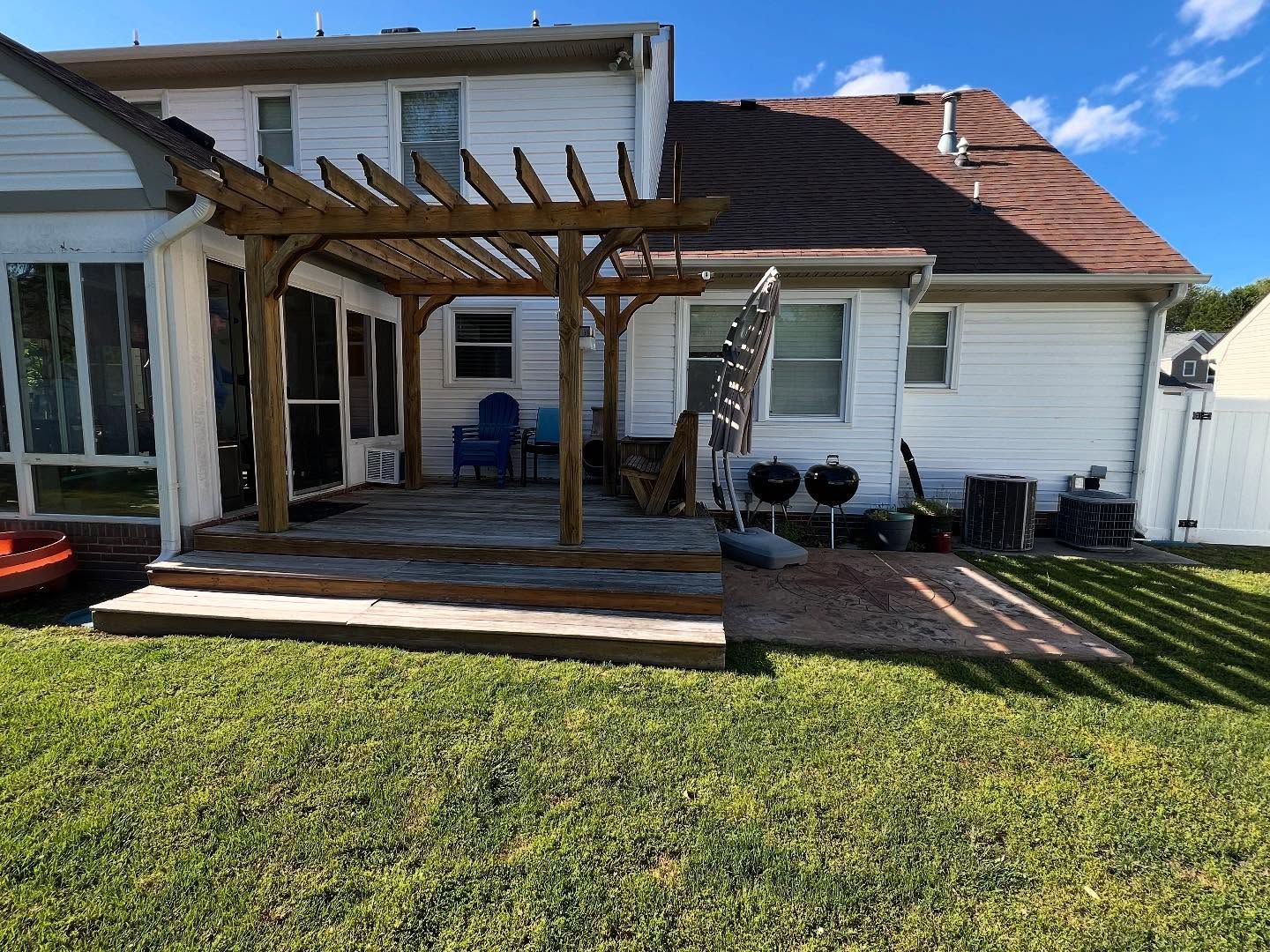 Backyard patio with wooden pergola, steps, and white house exterior beside a green lawn