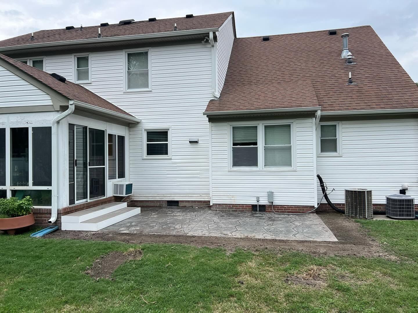 White house exterior with brown roof, screened porch, and small patio overlooking a grassy yard
