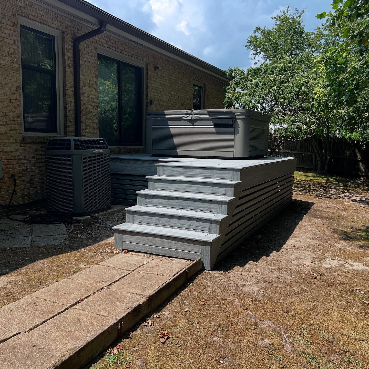 Backyard patio with steps leading to a raised hot tub beside a brick house