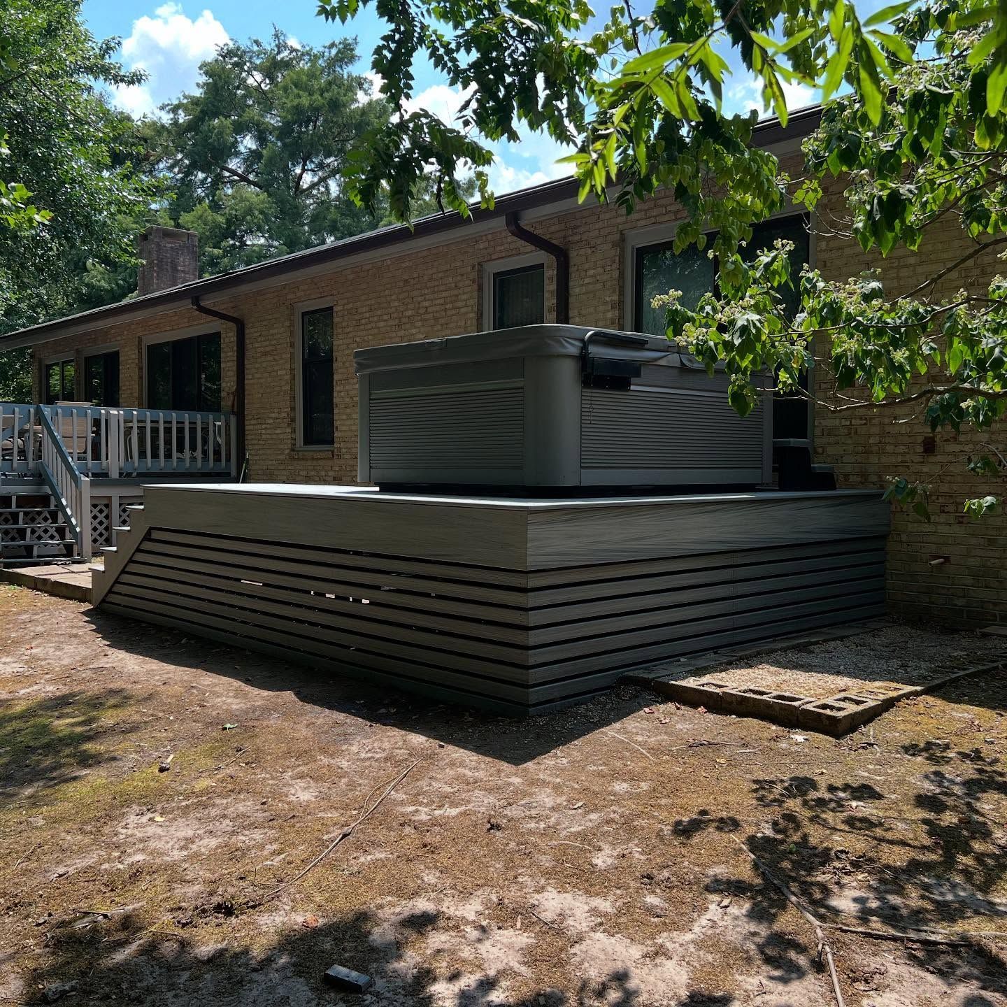 Backyard deck beside a brick house, with gray horizontal siding and trees overhead.