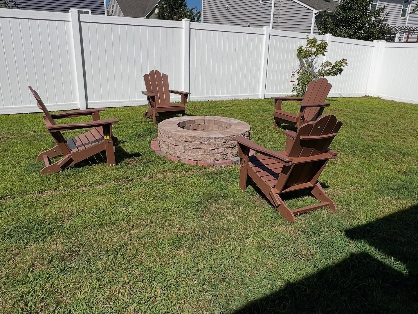Four wooden Adirondack chairs around a circular stone fire pit in a sunny backyard