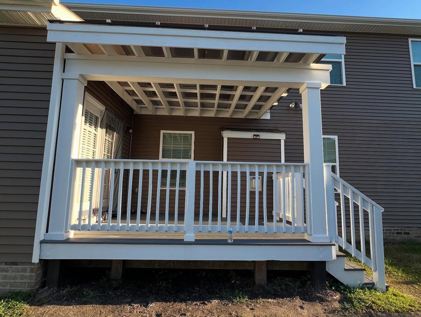 White front porch with railing and steps on a brick house, viewed from the yard