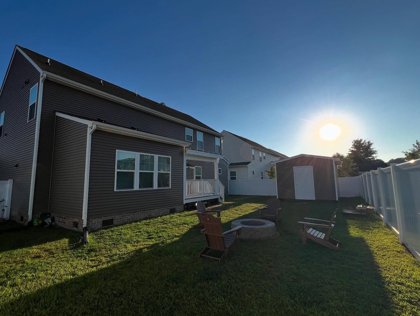 Suburban backyard with house, white fence, lawn chairs, and bright setting sun