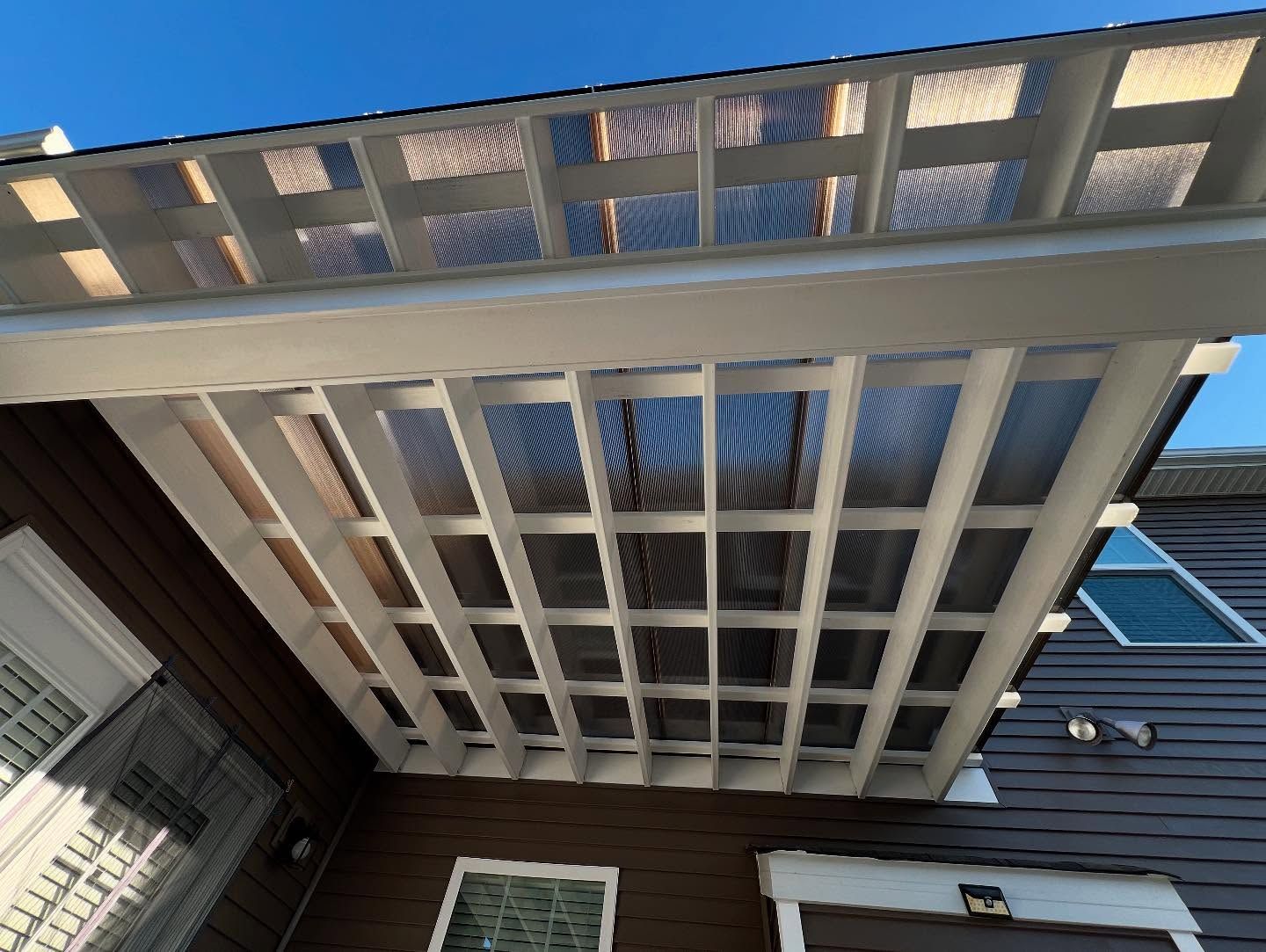Upward view of a white trellis over a brown house exterior with a blue roof edge.