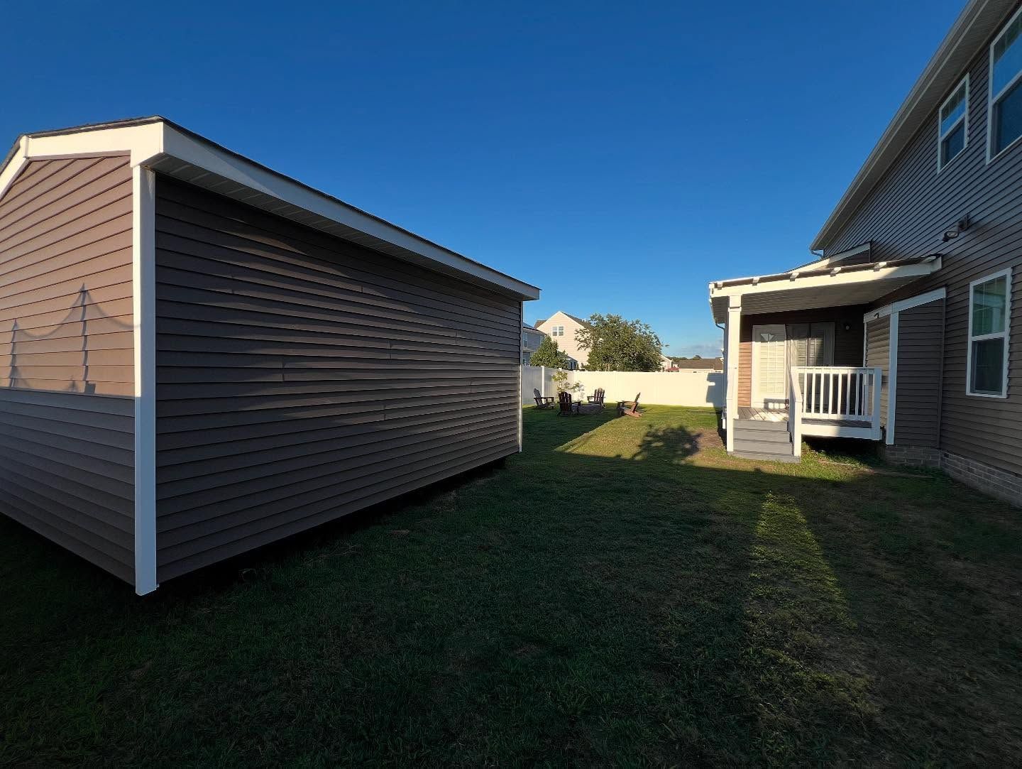 Two beige houses with a grassy side yard under a clear blue sky.