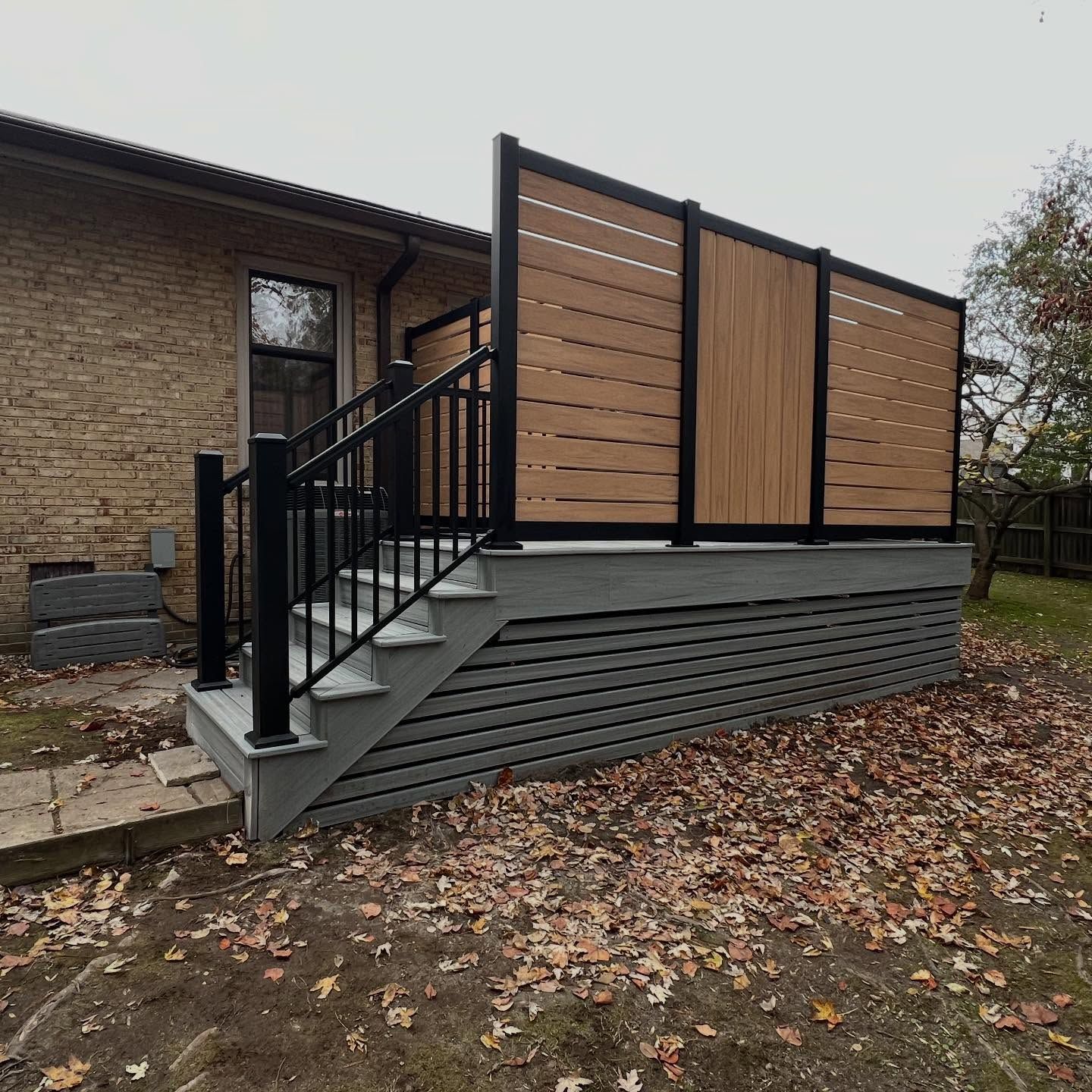 Modern deck ramp with black railings and wood privacy panels beside a brick house.