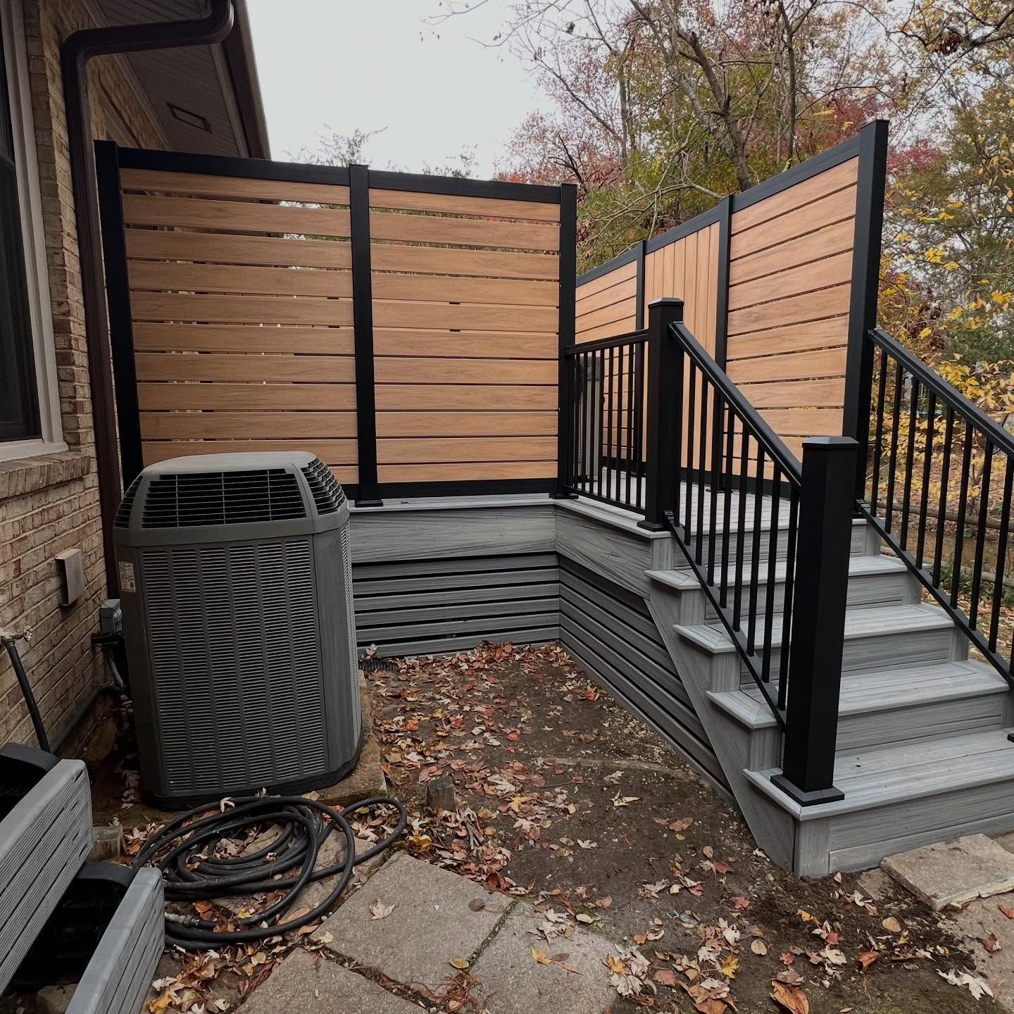 Backyard deck with gray stairs, black railing, tan privacy screens, and an outdoor AC unit