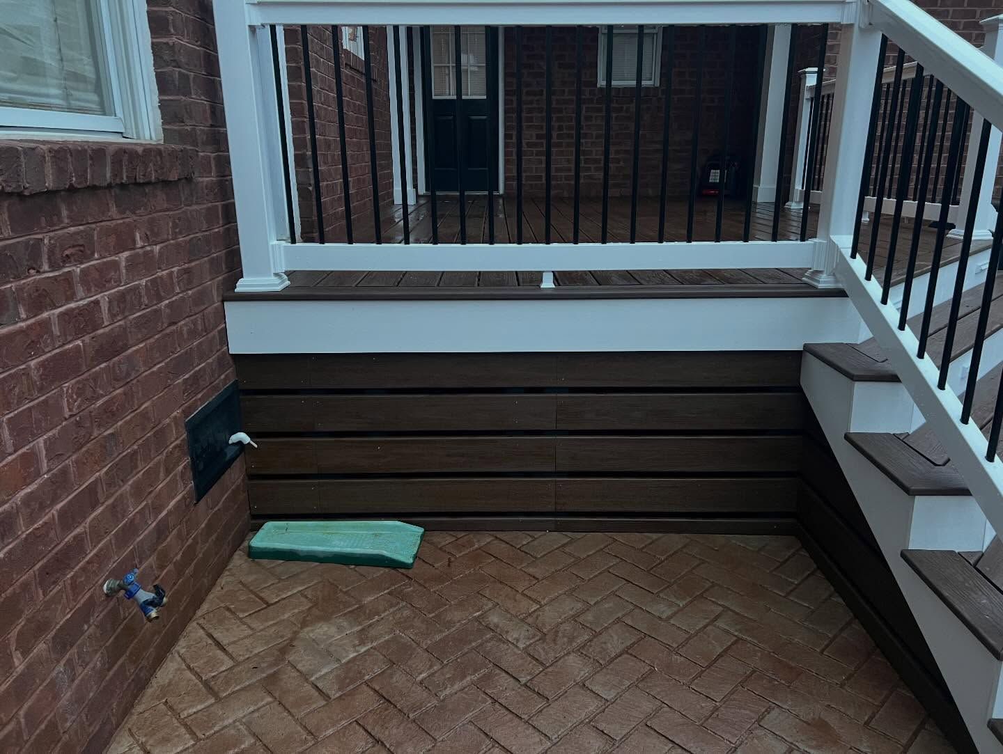 Brick porch with white railing, dark bench, and a small green cushion on a herringbone brick floor
