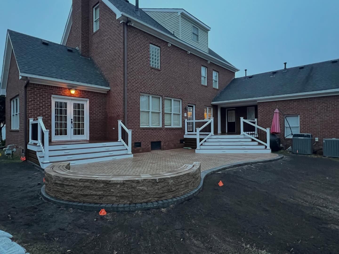 Brick house exterior with white decks and steps on a paved driveway at dusk